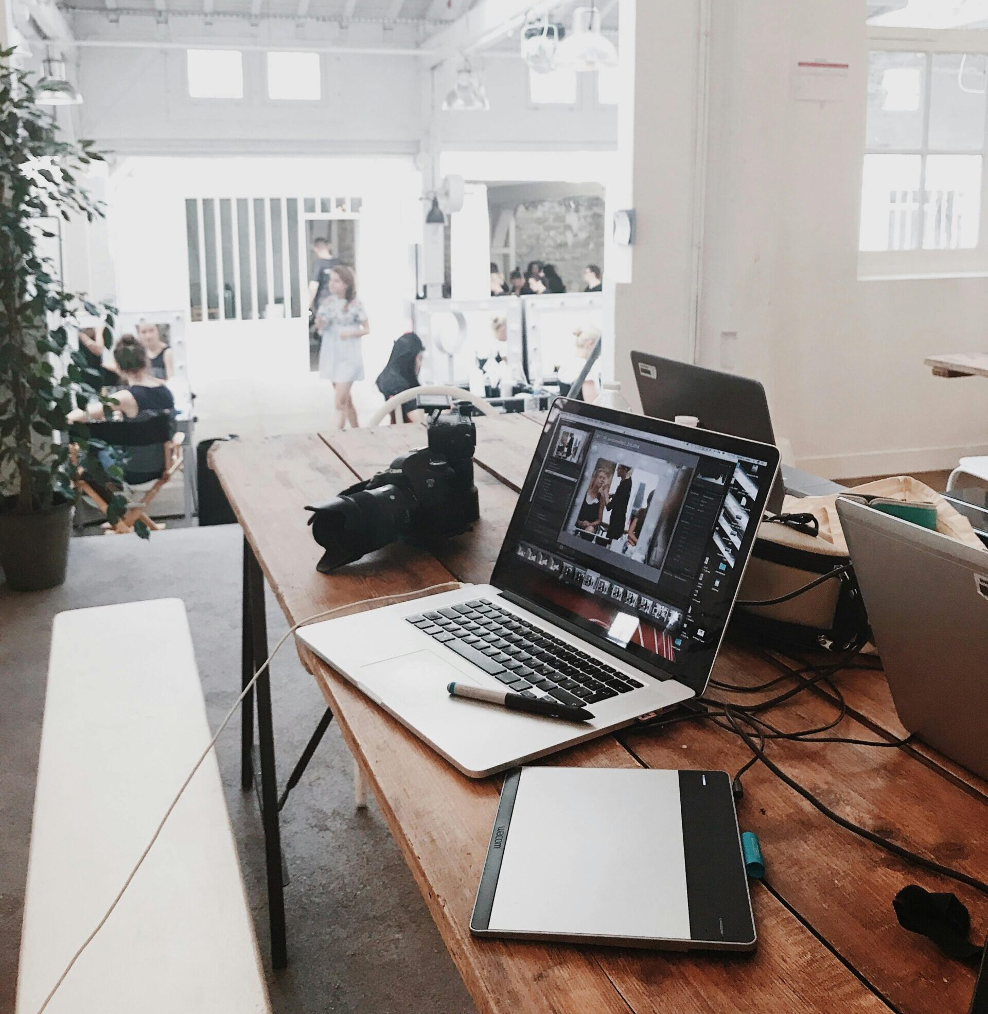 A bright, modern workspace featuring laptops, a camera, and a drawing tablet in an indoor office.